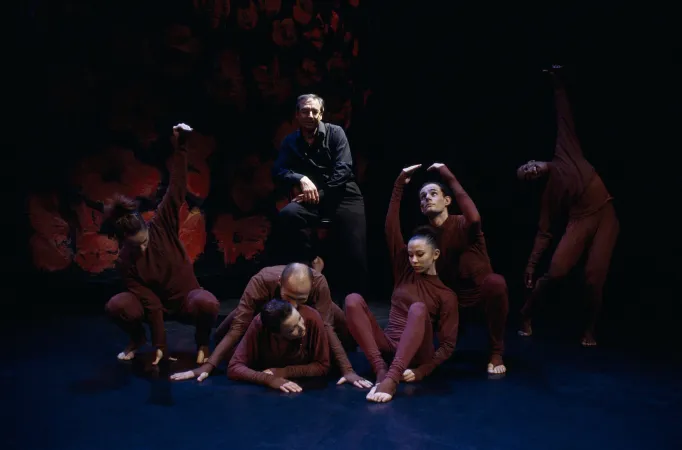 Spectacle Danser l'évolution : un homme sur scène habillé en noir et entouré de danseurs et danseuses habillés en bordeaux
